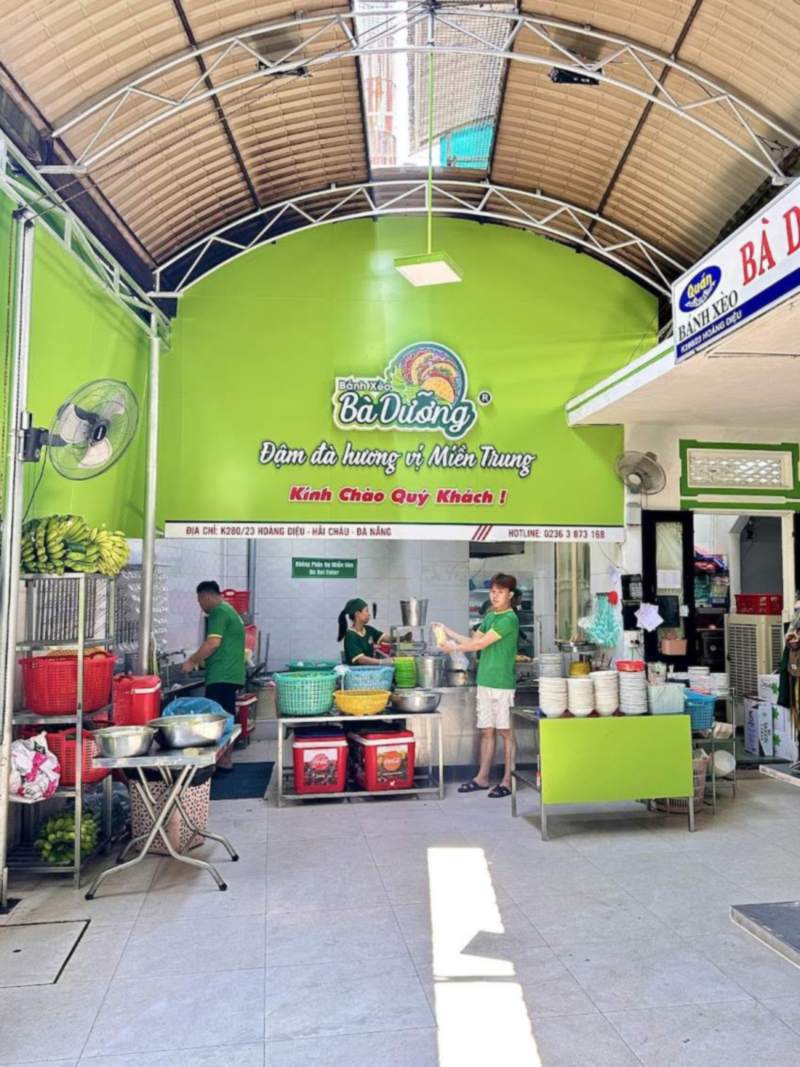 Gian bếp mở dưới bức tường xanh có logo Bà Dưỡng